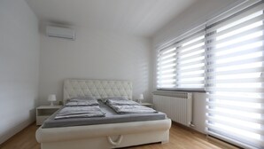 Un dormitorio con cama, mesitas de noche, un radiador y una ventana con persianas.