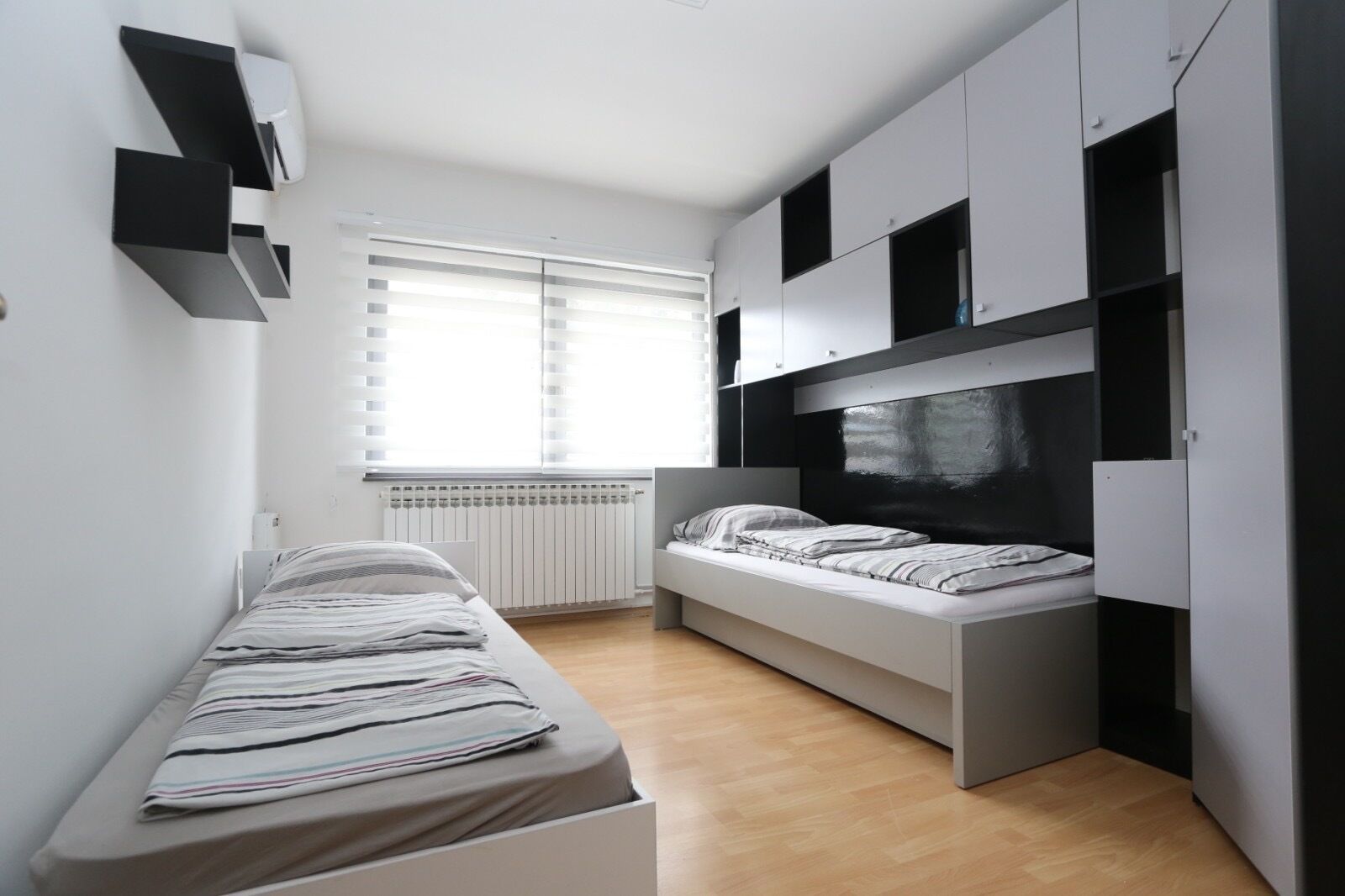 Un dormitorio pequeño con cama, almacenamiento integrado, radiador y ventana con persianas.