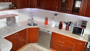 Una cocina con armarios de madera, un lavamanos de acero inoxidable, lavavajillas, hervidor de agua, cafetera y microondas.