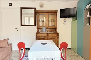 A room with a white table, two red chairs, a wooden cabinet, a television, and a door.