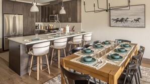 A modern kitchen with dark cabinets, stainless steel appliances, and a central island with bar stools. - New Build Condo with Shared Hot Tub (Big Sky)