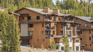 A multi-story wooden building with balconies, a garage, and a 'For Sale' sign. - New Build Condo with Shared Hot Tub (Big Sky)
