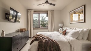 A bedroom with a bed, a dresser, a window with curtains, a ceiling fan, and a framed picture on the wall. - New Build Condo with Shared Hot Tub (Big Sky)