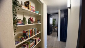 Ein Flur mit Bücherregal, gefüllt mit Büchern und Dekoration, der zu einem Zimmer mit Bett und Fenster führt.
