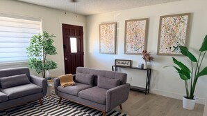 Ein Wohnzimmer mit einem grauen Sofa, einem Streifen Teppich und einer Tür.
