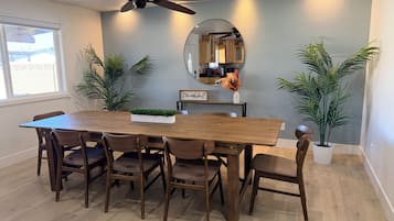 A dining area with a wooden table, six chairs, a ceiling fan, and potted plants.