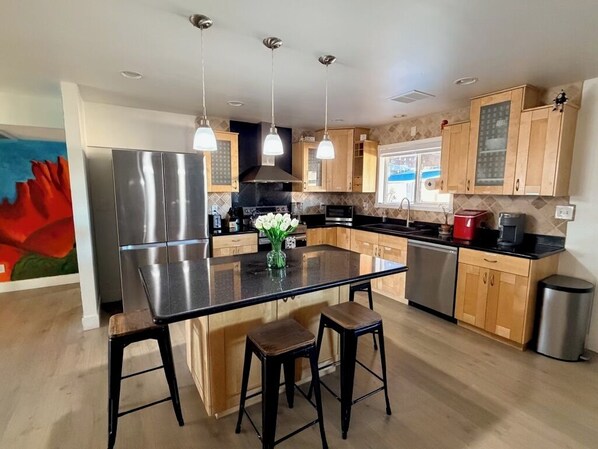A modern kitchen with a central island, stainless steel appliances, wooden cabinets, and pendant lighting. - Pool + Hot Tub Oasis, Family Retreat, Sleeps 7 (Chandler)