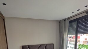 Et moderne soveværelse med en stor seng, et natbord, et sengebord og udsigt til bygninger gennem et stort vindue.