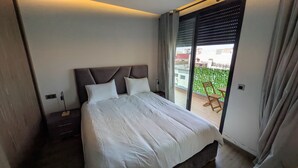 Et hotelværelse med en stor seng, et natbord, en lampe og udsigt til en balkon med en stol.