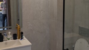 Et moderne badeværelse med et glasbadeværelse, et hvidt toilet og en vask med toiletartikler.