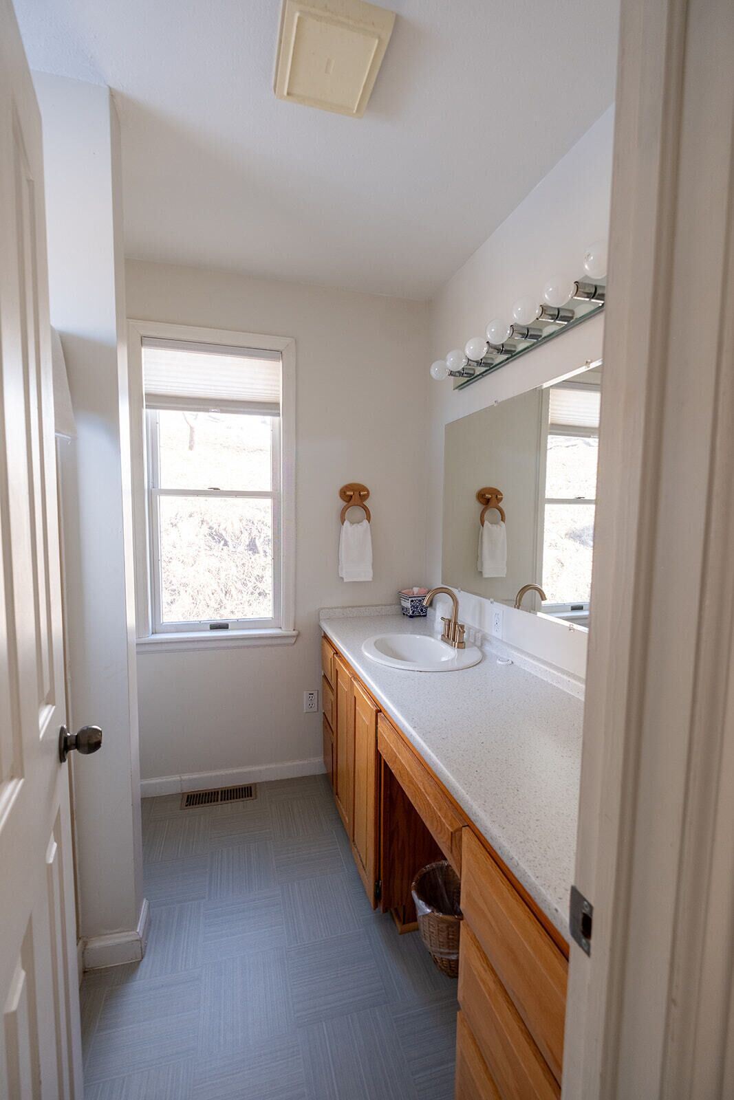 Un baño con ventana, lavamanos, espejo y muebles de madera.