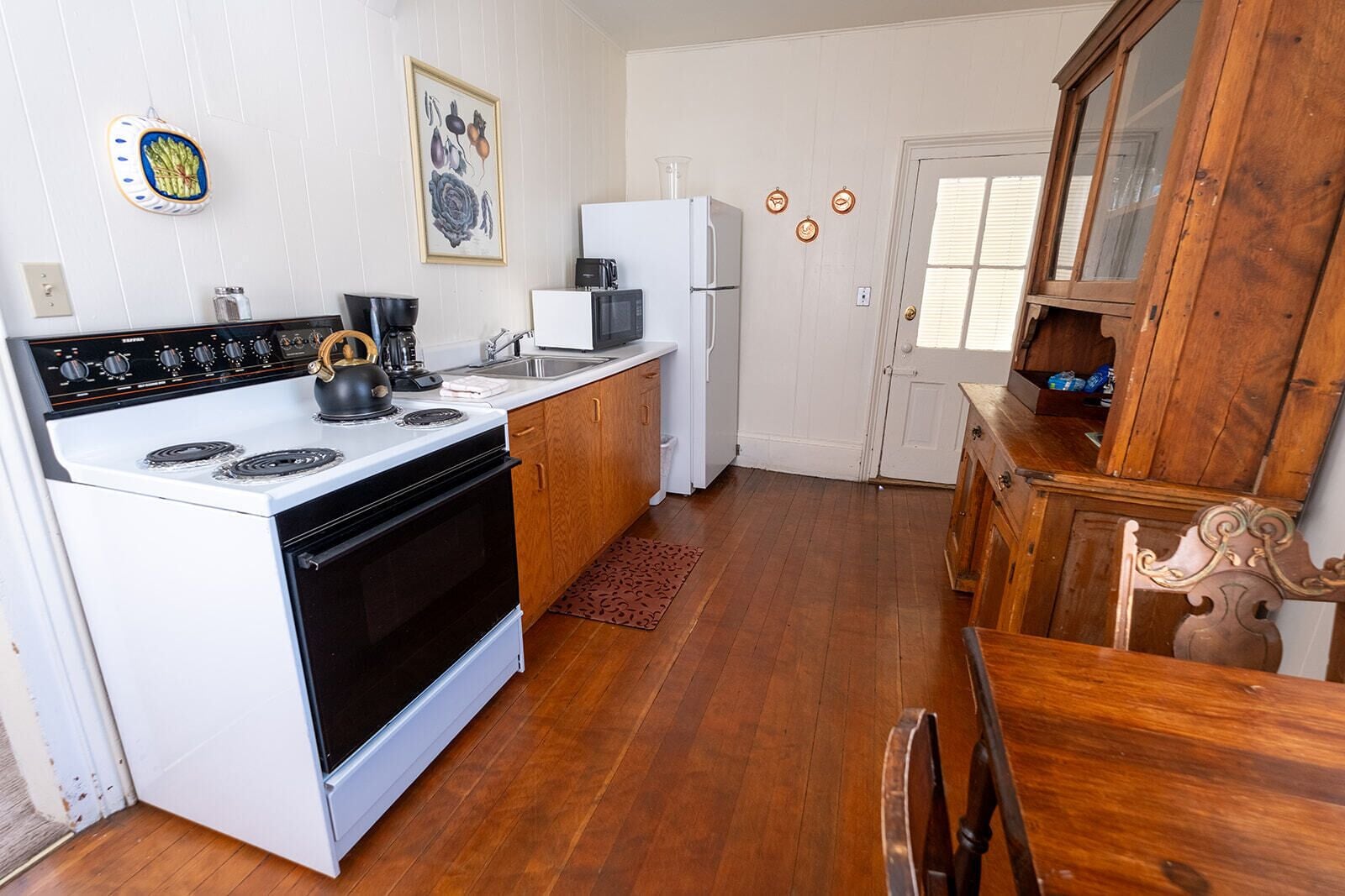 A compact kitchen with a stove, microwave, and refrigerator, wooden flooring, and a dining area with a table and chairs.