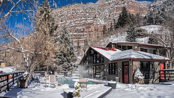 Una cabaña con piscina, rodeada de árboles y montañas cubiertas de nieve.
