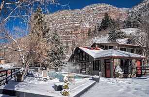 Una cabaña con piscina, rodeada de árboles y montañas cubiertas de nieve.
