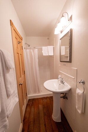 Une salle de bain avec une porte en bois, un lavabo blanc, une douche et un miroir.