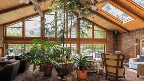 Una habitació àmplia amb grans finestres, bigues de fusta al sostre i moltes plantes en testos.