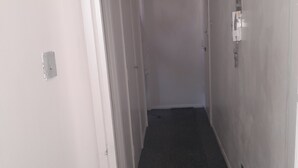 Un couloir étroit aux murs blancs, doté d’un sol recouvert de moquette et d’une porte au fond.