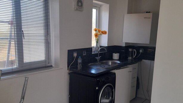 Une cuisine compacte équipée d’un lave-linge, d’un évier et d’une fenêtre avec des stores.