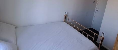 A bedroom with a bed, a door, and a hanging light fixture.