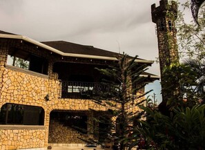 A stone building with a balcony, a staircase, and a tower. - Jaco Castle by Rey (Jacó)