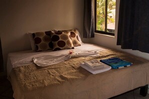 A bed with a beige bedspread, two pillows with a circular pattern, a white towel, and a blue bag on the bed. - Jaco Castle by Rey (Jacó)