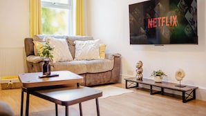 Un salon comprenant un canapé, une table basse, un téléviseur fixé au mur et une petite table ornée d’objets décoratifs.