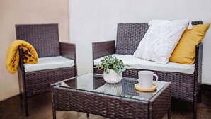Un canapé en osier avec des coussins, une table basse en verre ornée d’une plante et d’une tasse, et un plaid jaune jeté sur une chaise.
