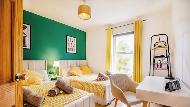 Une chambre d’hôtel avec deux lits, un bureau, une chaise, une lampe et une fenêtre avec des rideaux.