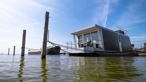 Una estructura flotante con un pequeño edificio, posiblemente una sala de control u oficina, y un gran barco amarrado cerca.