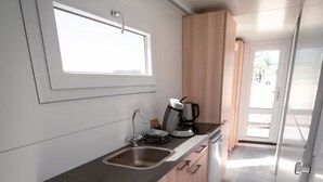 Una cocina compacta con ventana, un lavamanos, una cafetera y un cubo de basura.