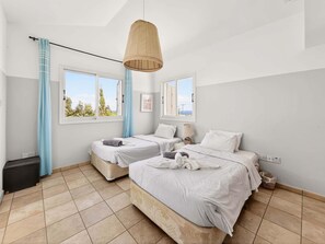 A bedroom with two beds, a hanging light fixture, and a view of the outdoors. - Villa Marilena: Spacious Protaras Villa with Pool (Protaras)