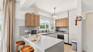 Una cocina moderna con una isla central, taburetes de madera, microondas, tostadora y vistas al exterior.