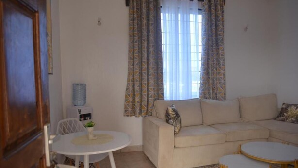Una sala de estar con un sofá color beige, dos mesitas redondas y cortinas estampadas.
