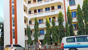 Un edificio de varios pisos con balcones, un patio empedrado y vehículos estacionados.