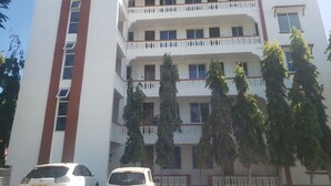 Un edificio de varios pisos con balcones, coches aparcados y árboles.