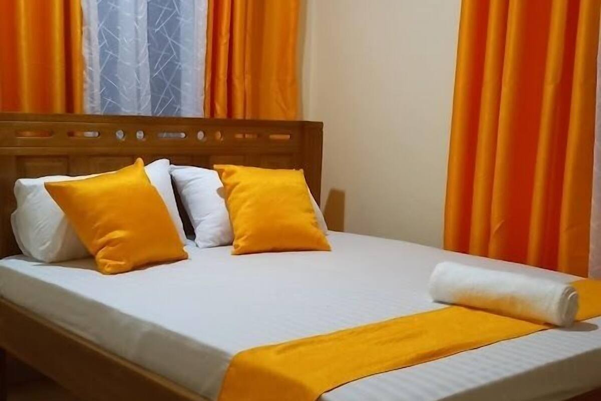 Uma cama com cabeceira de madeira, roupa de cama branca e duas almofadas laranja.