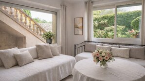 A room with a staircase, two beds with matching bedding, a table with a vase of flowers, and a window with a view of greenery. - Le Mas d'Eylieux - Les Citronniers - Les Citronniers - Escapade in Southern Ardèche (Saint-Montan)