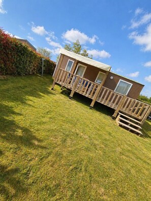 A two-story mobile home with a balcony, a fenced yard, and a hedge. - Cottage Champêtre n°1 à Angliers - 6p (Angliers)