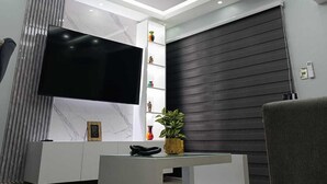 A modern living room with a flat-screen TV, a white entertainment unit, a dark sliding door, and recessed ceiling lighting. - Gray House, Spacious and elegant apt., swimming pool, GYM (Punta Cana)
