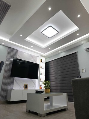 A modern living room with a flat-screen TV, a white entertainment unit, a dark sliding door, and recessed ceiling lighting. - Gray House, Spacious and elegant apt., swimming pool, GYM (Punta Cana)