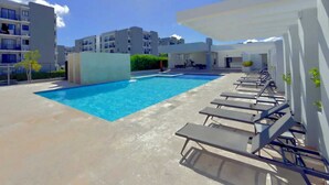A swimming pool with lounge chairs, surrounded by buildings. - Gray House, Spacious and elegant apt., swimming pool, GYM (Punta Cana)