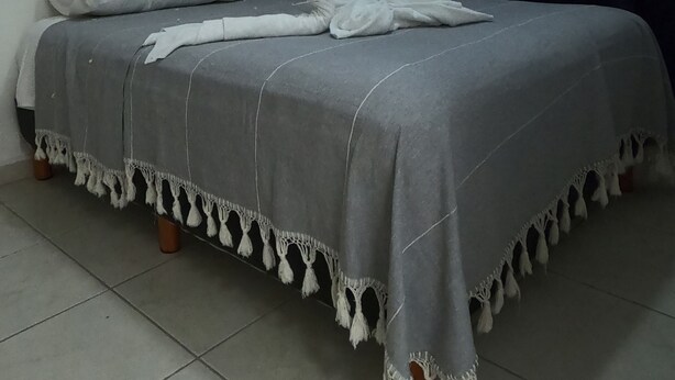 A bedroom with a bed, pillows, a wall-mounted air conditioner, a small shelf, and a curtain. - Casa Atardecer (Playa del Carmen) Los Olivos (Playa del Carmen)