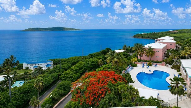Ett semesterhotell med en swimmingpool, frodig grönska och utsikt över havet.