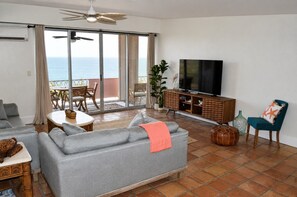 Ett vardagsrum med en grå soffa, en tv och en balkong med utsikt över havet.