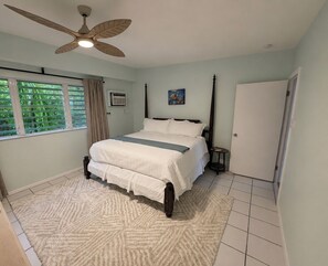 Ein Schlafzimmer mit einem Bett, einem Deckenventilator, einem Fenster mit Vorhängen und einer Tür.