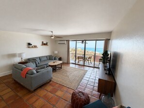 Ein Wohnzimmer mit einer Couch, einem Couchtisch und Blick auf den Strand durch große Fenster.