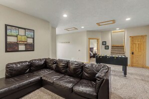 A room with a sectional leather sofa, a foosball table, and a wall-mounted artwork.