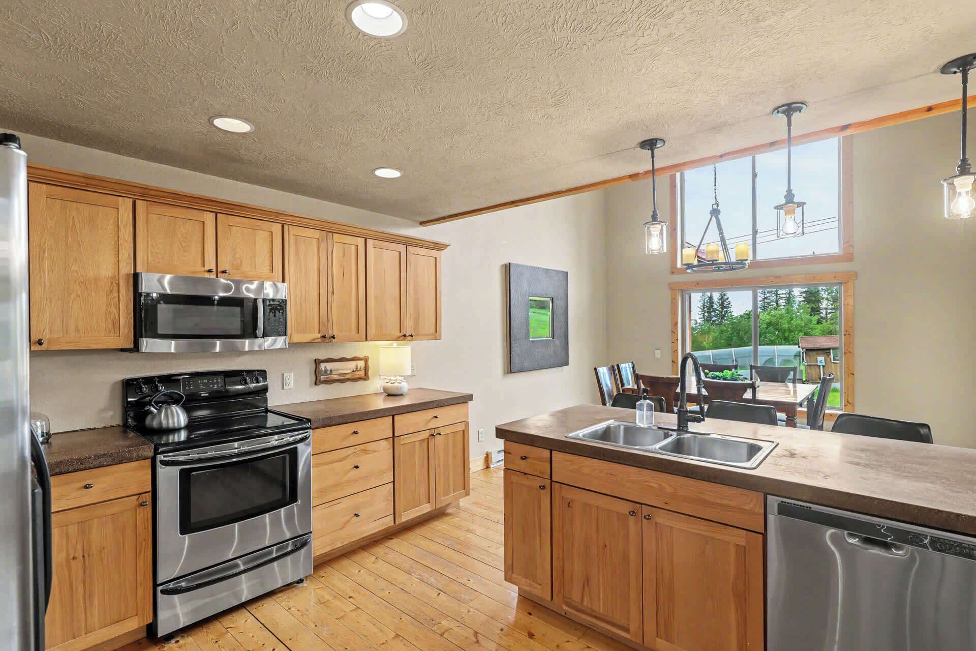 A kitchen with wooden cabinets, stainless steel appliances, and a large window overlooking a garden.