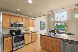 A kitchen with wooden cabinets, stainless steel appliances, and a large window overlooking a garden. - Homestake Slopeside Chalet at Terry Peak (Lead)