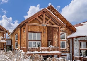 A wooden cabin with a balcony, large windows, and a sign reading 'Homestay.' - Homestake Slopeside Chalet at Terry Peak (Lead)